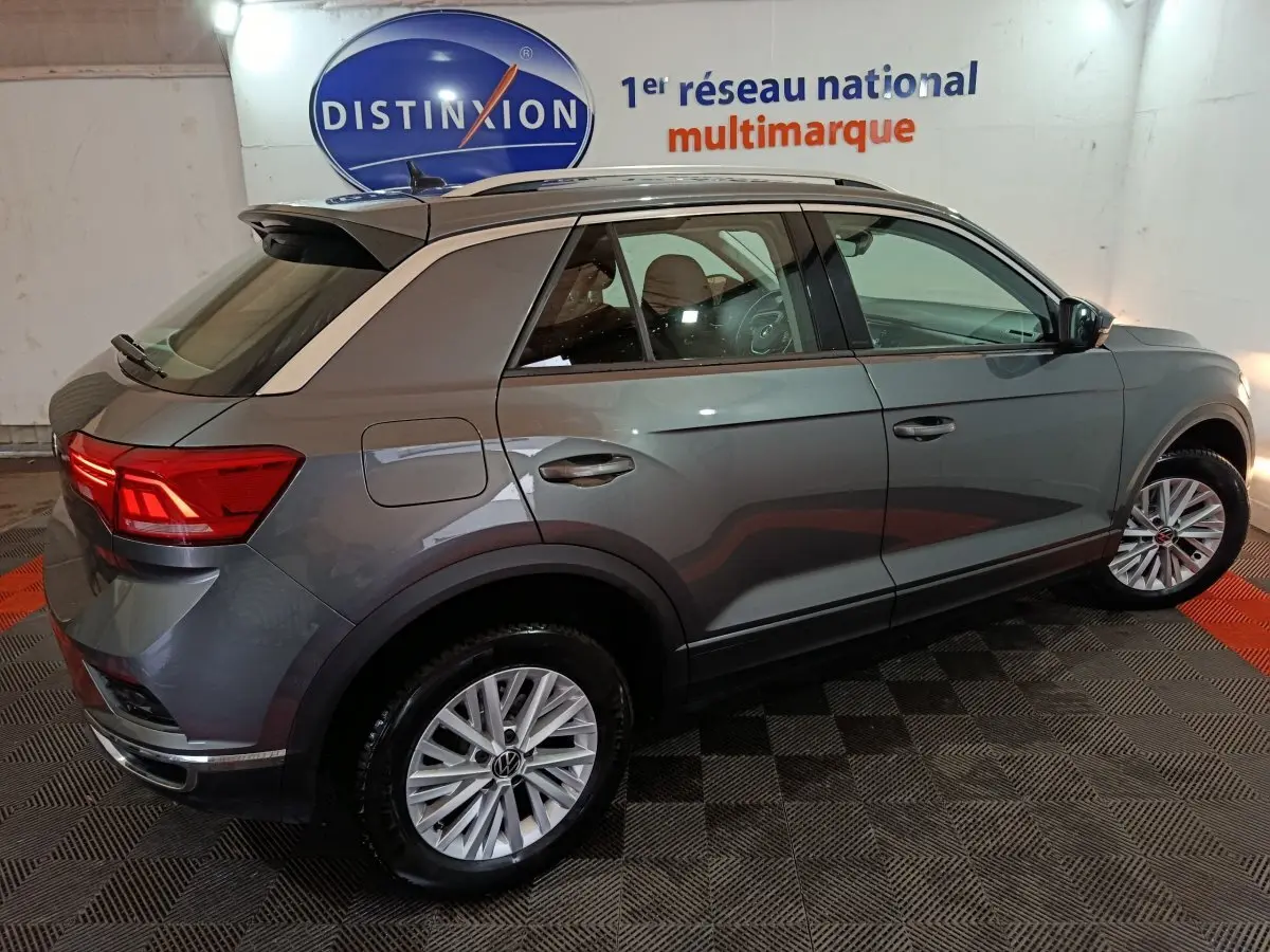 Vue 3/4 arrière droite d’un Volkswagen T-Roc gris foncé 2021 avec jantes alliage et feux arrière LED allumés.