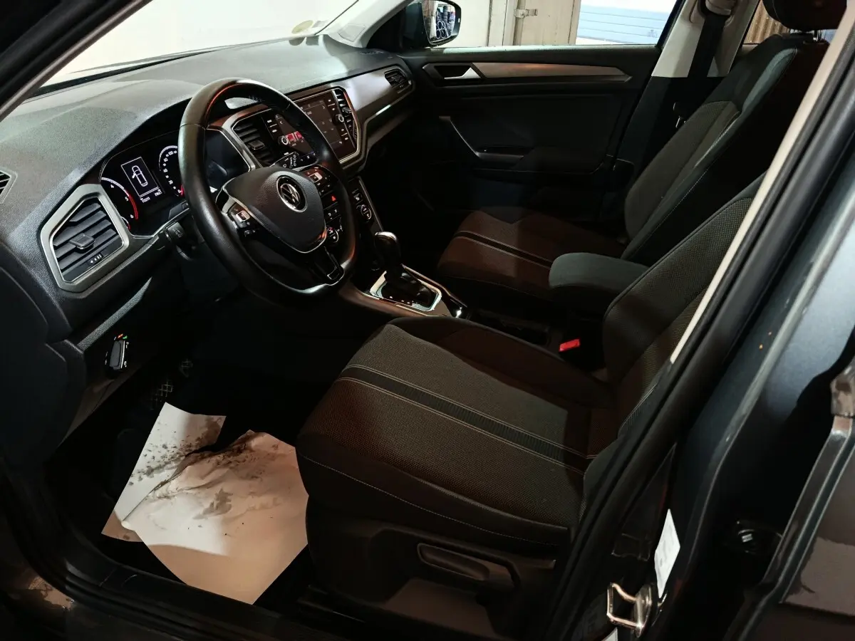 Vue intérieure côté conducteur du Volkswagen T-Roc gris foncé, avec tableau de bord digital et volant cuir multifonctions.