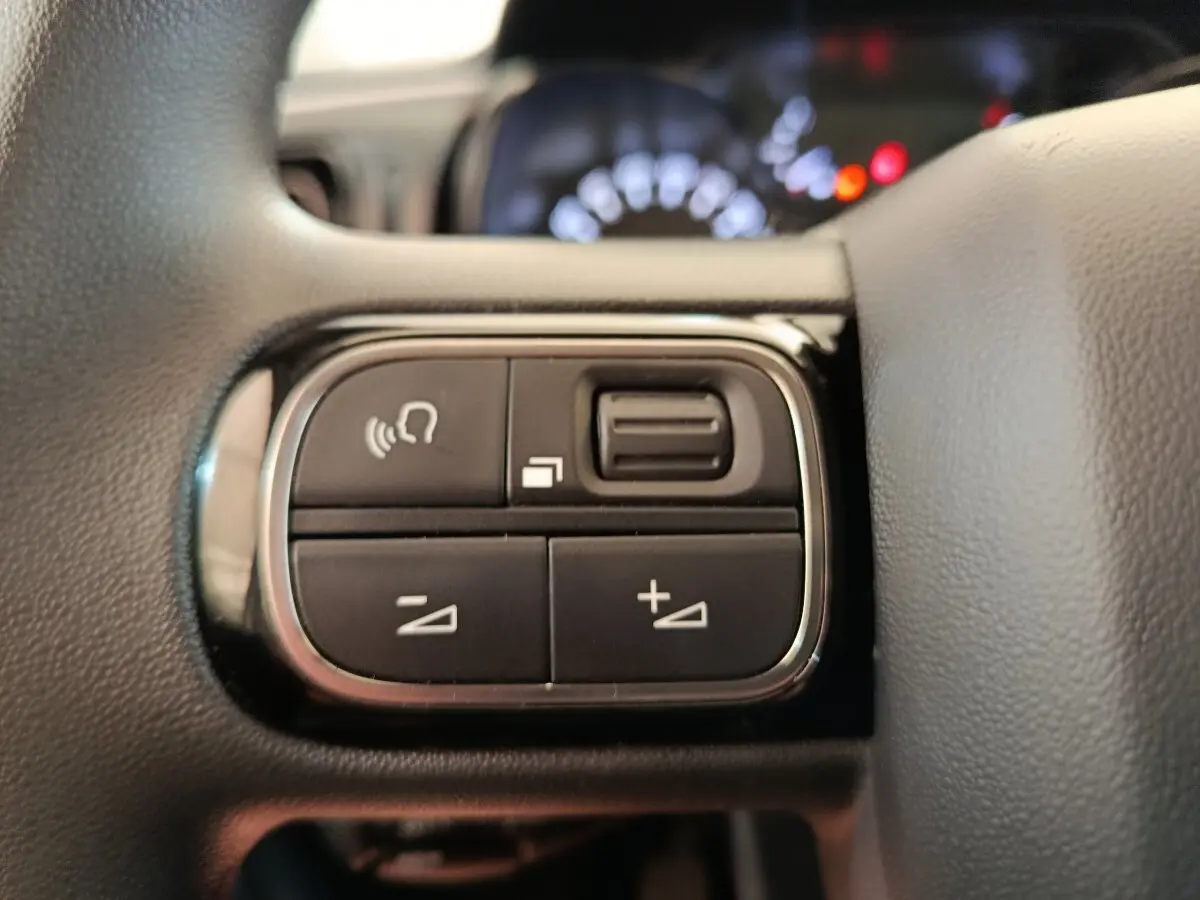 Gros plan sur les commandes au volant à gauche du tableau de bord d’une Citroën C3 blanche, version 2020.