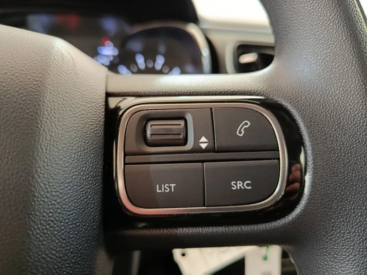 Gros plan sur les commandes gauche du volant noir de la Citroën C3 blanche, boutons pour téléphone et liste audio.