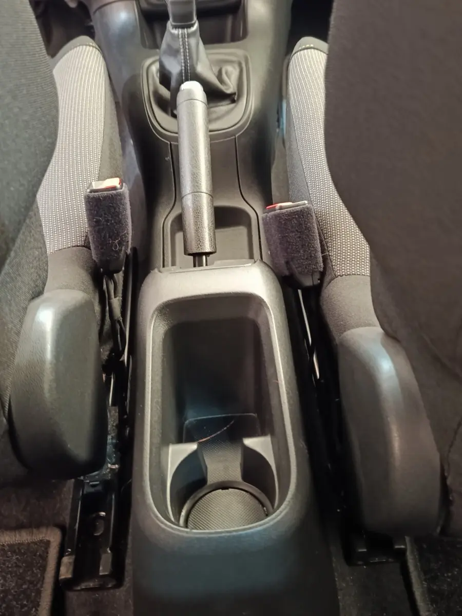 Vue rapprochée de la console centrale noire entre les sièges avant gris d'une Citroën C3 blanche, avec frein à main et porte-gobelet.
