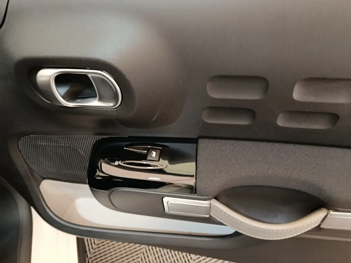 Détail de la porte intérieure côté conducteur de la Citroën C3 blanche, avec poignée argentée et commandes de vitre.