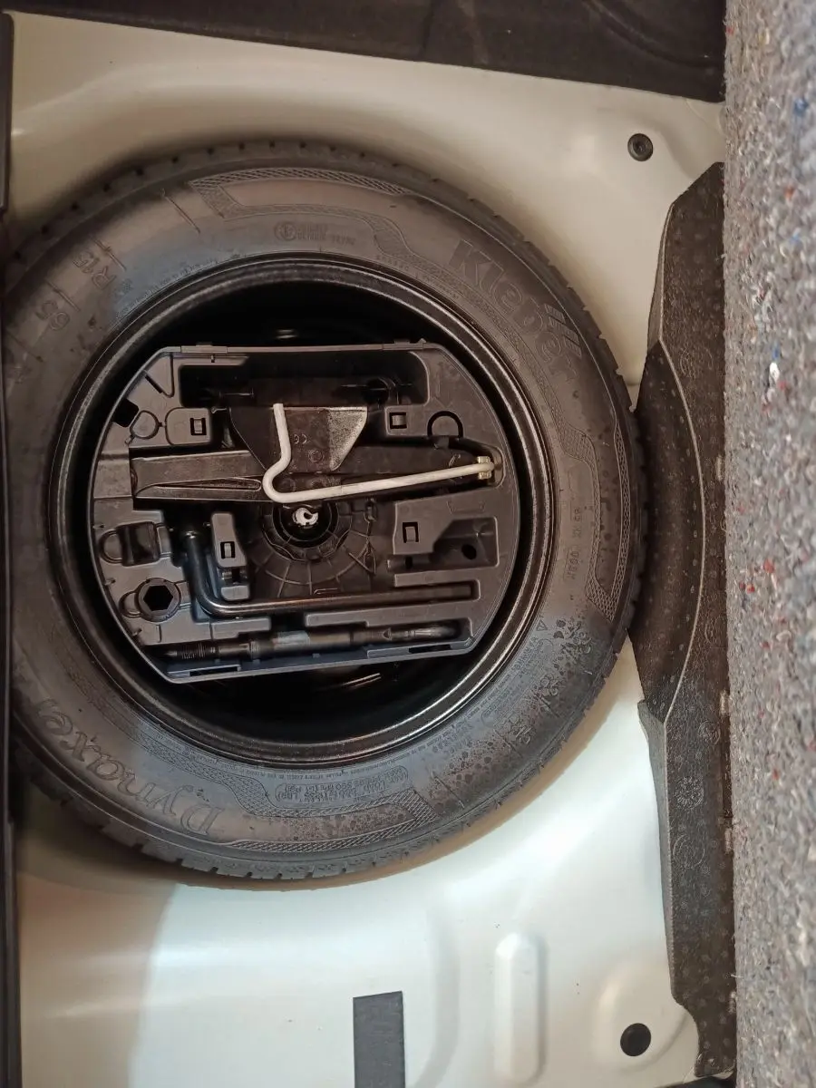 Vue rapprochée de la roue de secours noire et de ses outils, logée dans le coffre blanc d'une Citroën C3 2020.