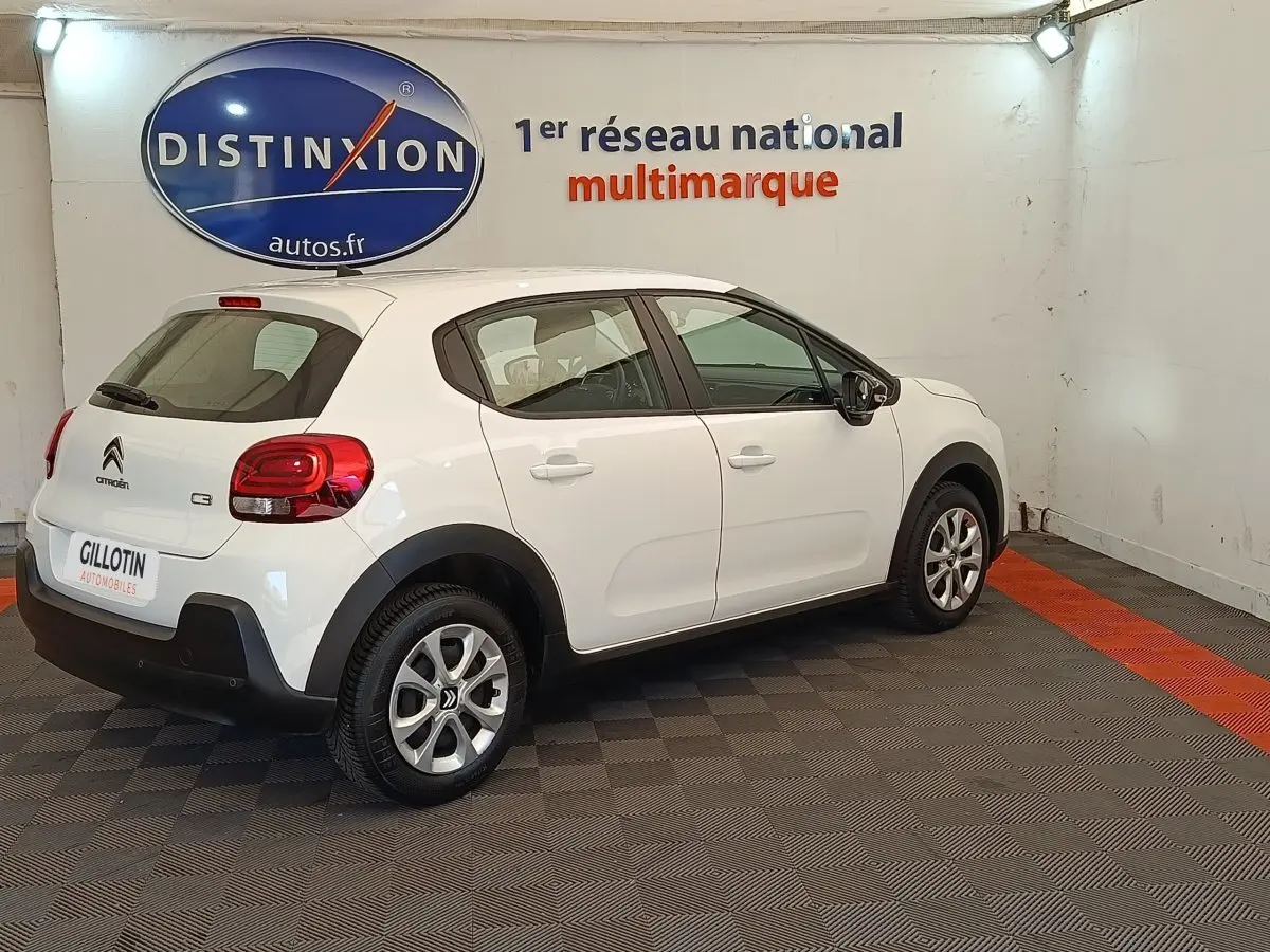 Vue 3/4 arrière droite d'une Citroën C3 blanche 2020 dans un showroom avec logo Distinxion en arrière-plan.