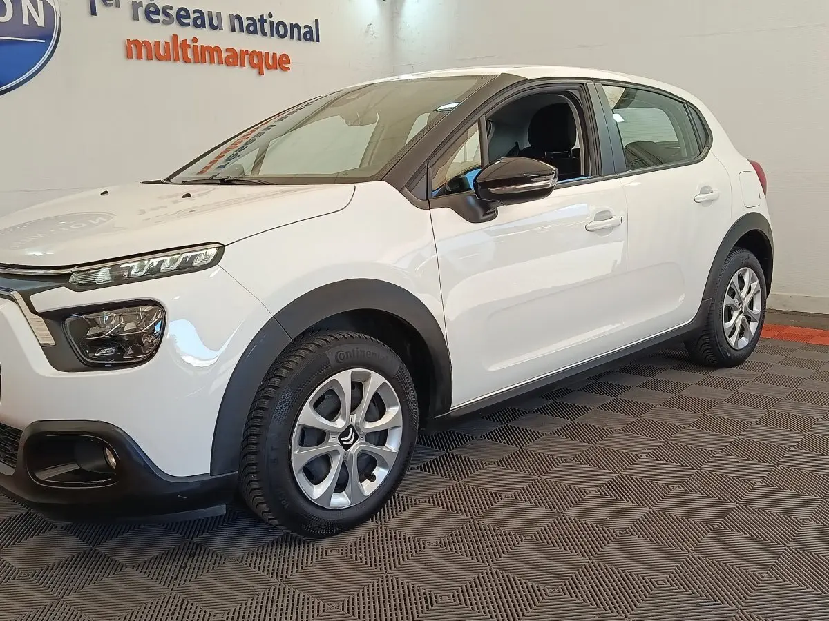 Vue 3/4 avant droite d'une Citroën C3 blanche avec jantes alliage et rétroviseurs noirs dans un showroom.