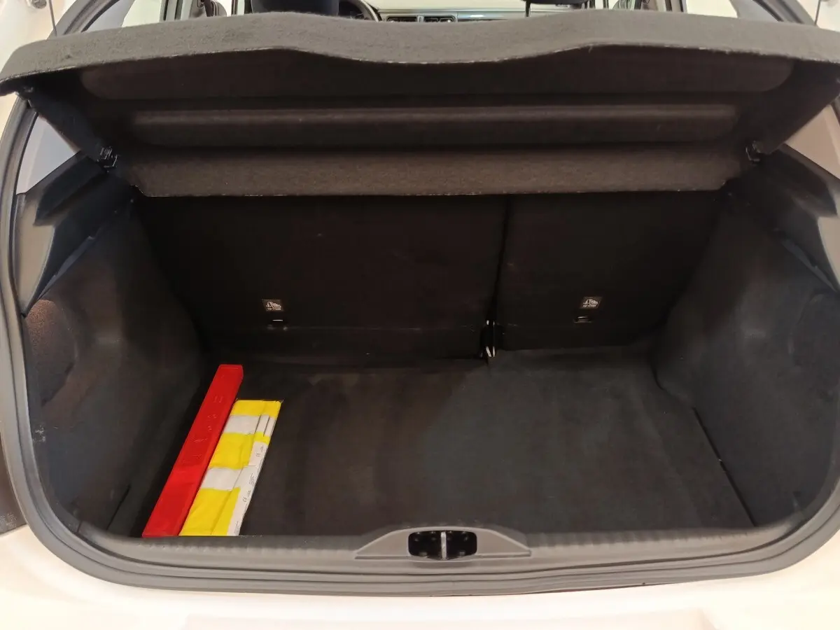 Coffre ouvert d’une Citroën C3 blanche, vue arrière, montrant un espace de rangement avec triangle de sécurité et gilet jaune.