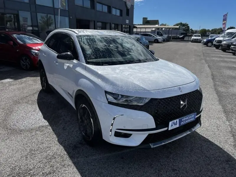 DS7 Crossback blanc vu en 3/4 avant droit, avec calandre noire distinctive et jantes foncées, sur parking extérieur.