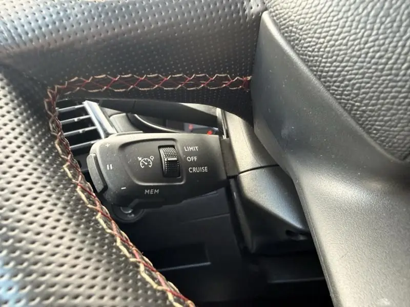 Gros plan sur la commande de régulateur de vitesse noire avec marquages blancs, entourée du volant en cuir noir sur DS7 Crossback blanc.