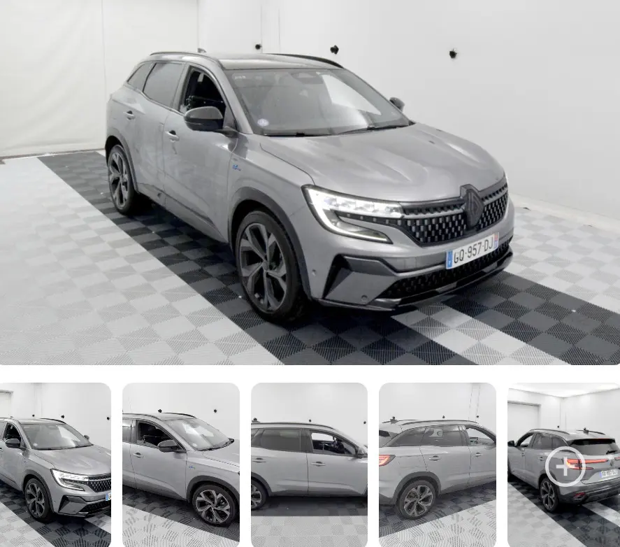 Vue 3/4 avant du Renault Austral gris avec jantes aluminium et barres de toit visibles en intérieur studio.