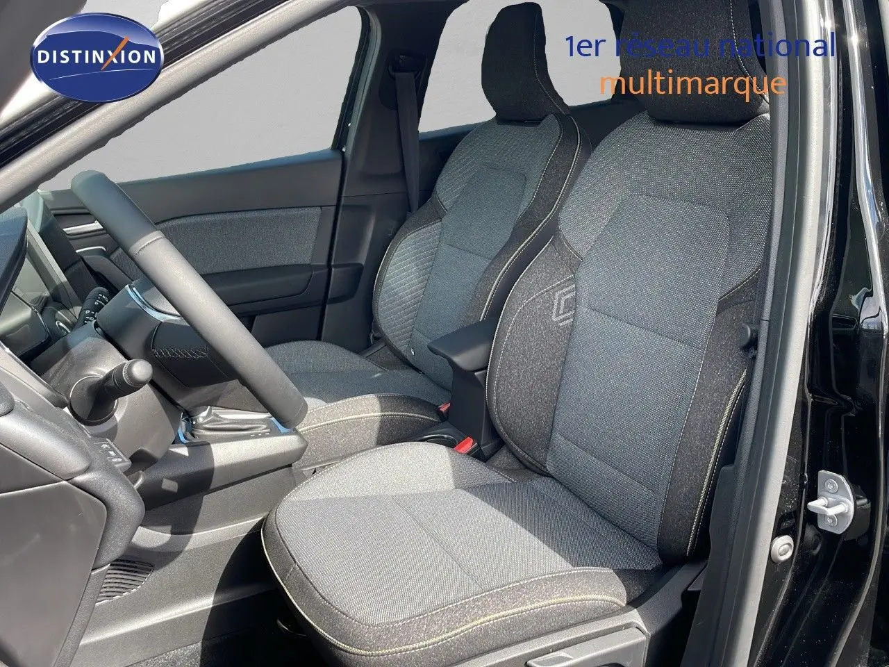 Vue intérieure côté conducteur du Renault Captur 2025, sièges tissu gris avec surpiqûres contrastées, portière noire ouverte.