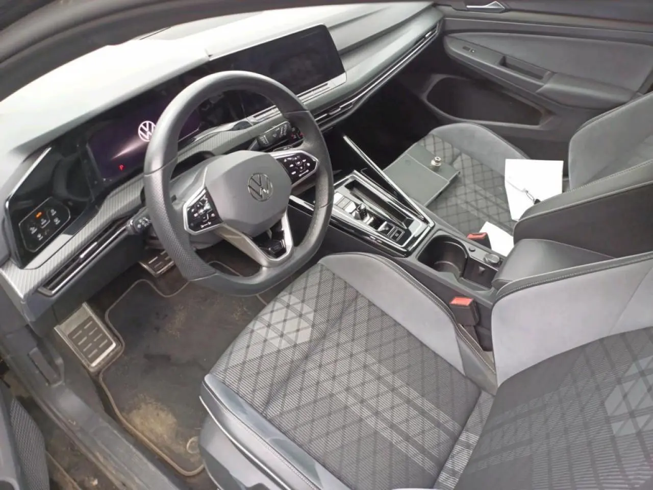 Vue intérieure côté conducteur de la Volkswagen Golf 8 R-Line 2024, sièges tissu noir et tableau de bord digital.