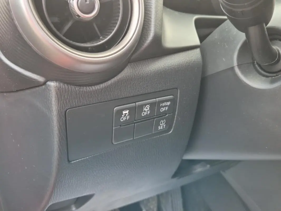 Gros plan sur les commandes de sécurité et l'aération côté gauche du tableau de bord noir d'une Mazda2 rouge 2021.