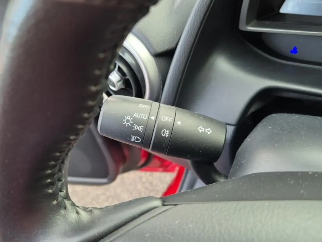 Gros plan sur la commande des feux et clignotants à gauche du volant cuir dans l'habitacle d'une Mazda2 rouge 2021.