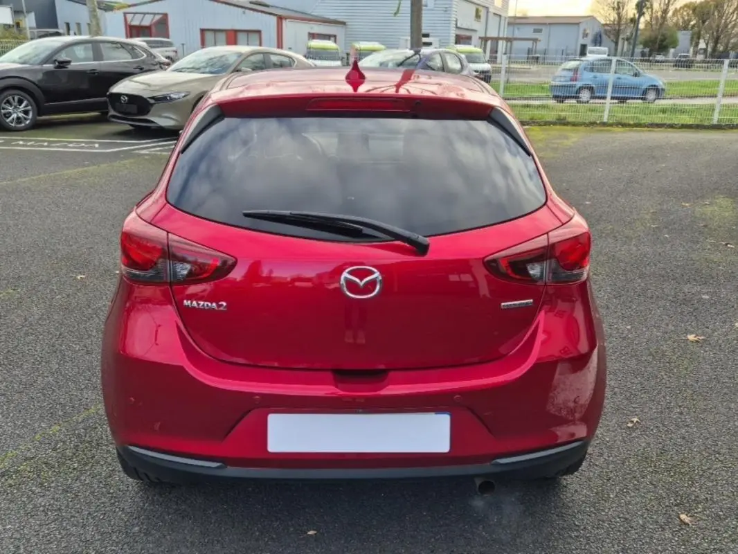 Vue arrière d'une Mazda2 rouge brillante avec vitres surteintées et logo Mazda bien visible.