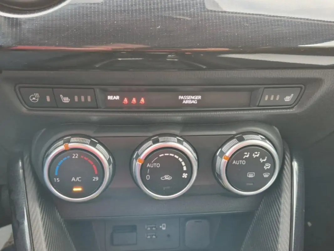 Vue rapprochée des commandes de climatisation automatique et chauffage des sièges d'une Mazda2 rouge 2021.