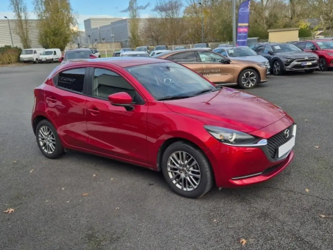 Vue 3/4 avant gauche d'une Mazda2 rouge brillante avec jantes aluminium et vitres surteintées sur parking.