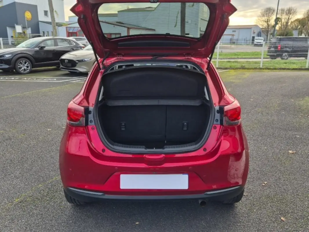 Vue arrière d'une Mazda2 rouge 2021 avec coffre ouvert sur un parking extérieur.