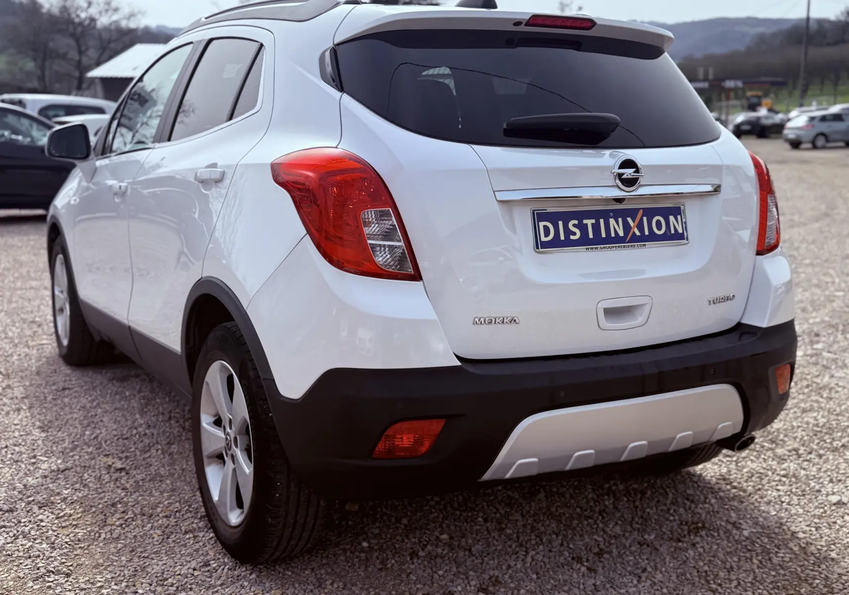 Vue 3/4 arrière droite d'un Opel Mokka X blanc avec feux arrière rouges et plaque d'immatriculation Distinxion.