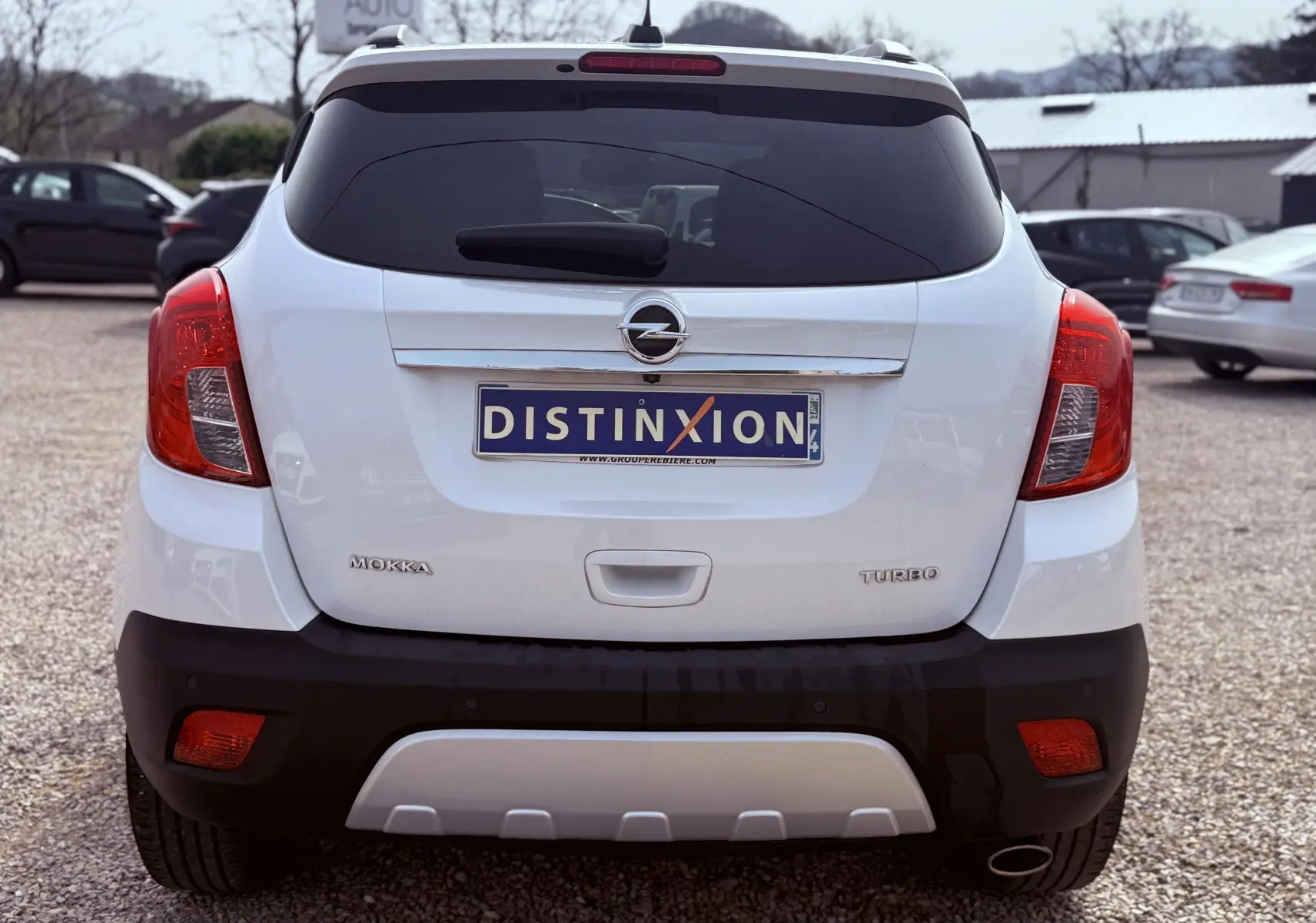 Vue arrière d'un Opel Mokka X blanc avec feux rouges et plaque d'immatriculation Distinxion visible.