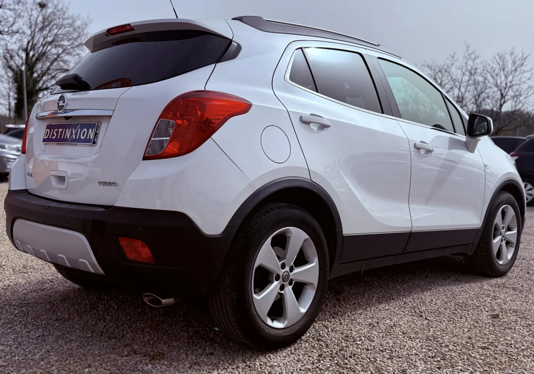 Vue 3/4 arrière droite d'un Opel Mokka X blanc avec jantes alliage et vitres teintées sur parking.