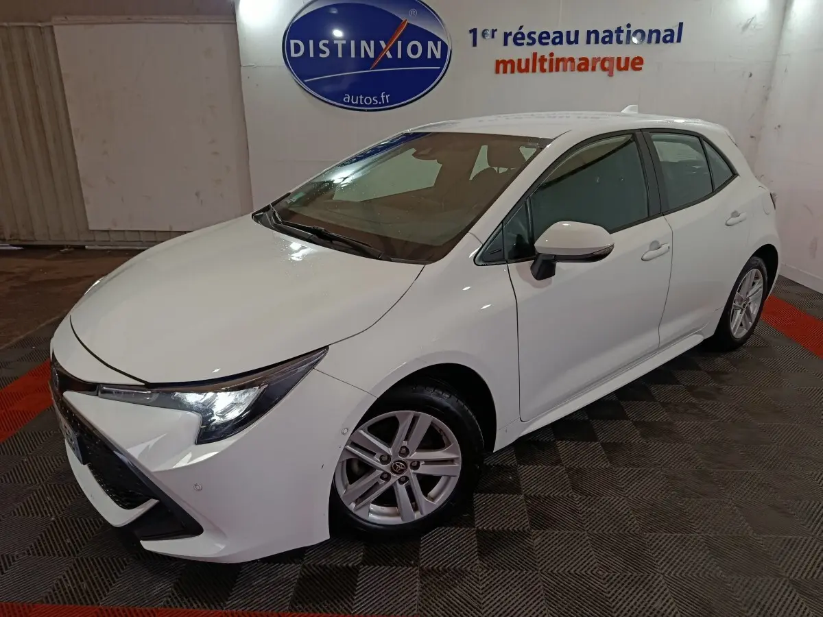 Toyota Corolla hybride blanche vue en 3/4 avant droit, avec phares LED et jantes alliage visibles.