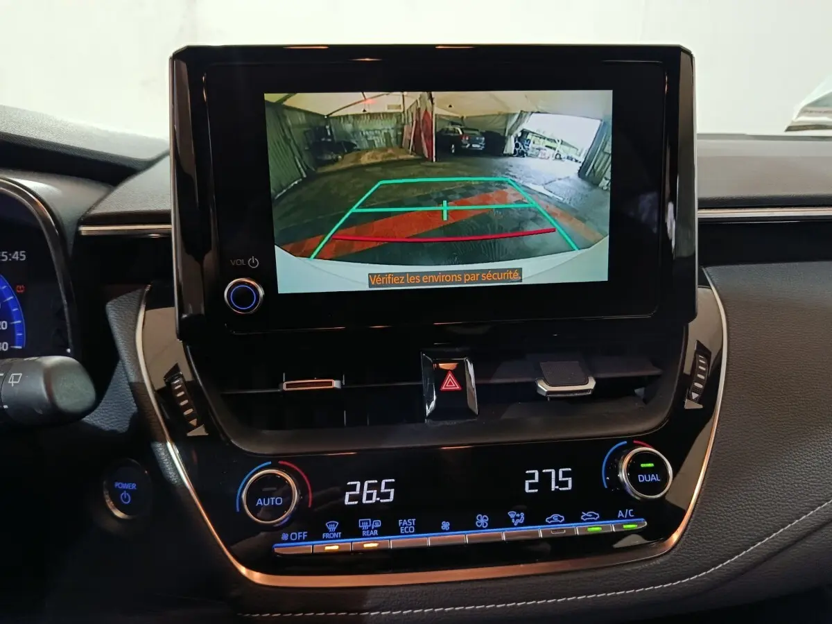 Vue intérieure du tableau de bord de la Toyota Corolla hybride blanche, avec écran de caméra de recul et commandes climatisation.