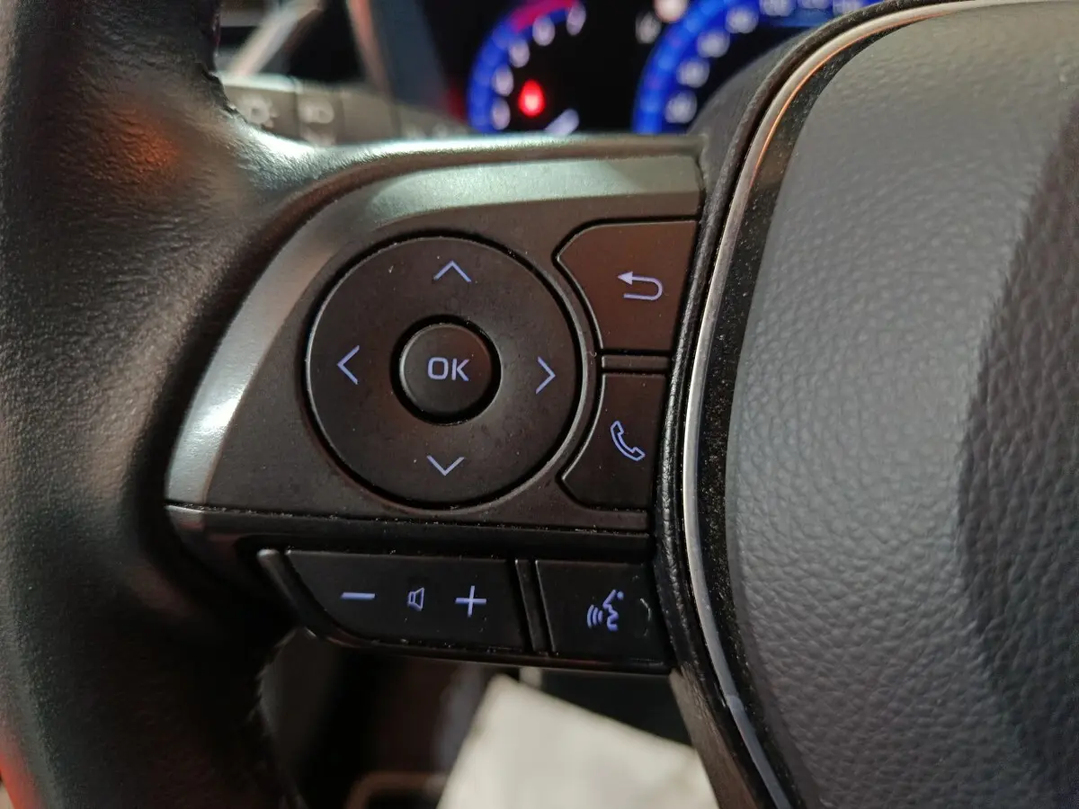 Gros plan sur les commandes au volant côté gauche de la Toyota Corolla hybride blanche, avec boutons multifonctions rétroéclairés.