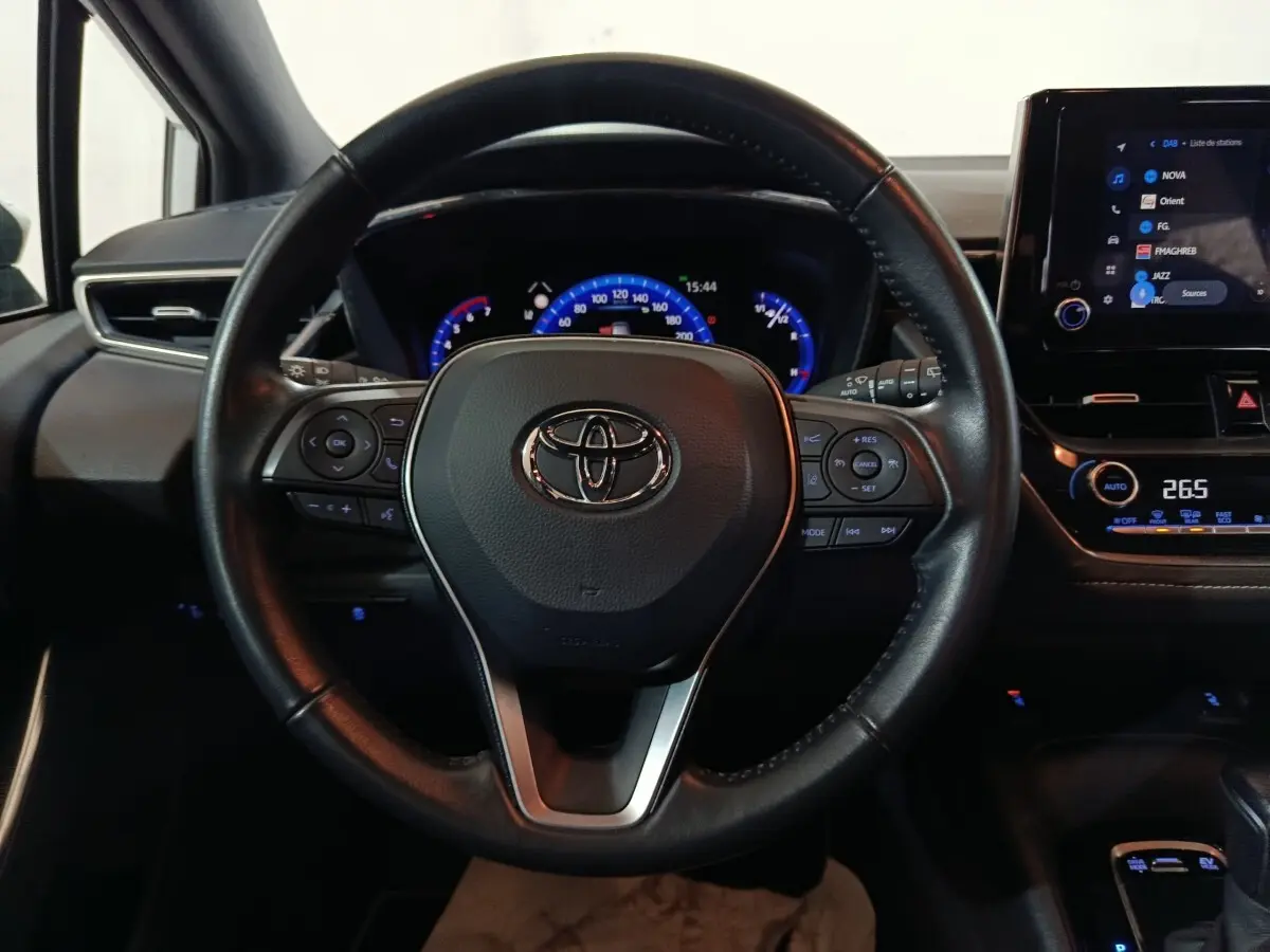 Vue intérieure centrée sur le volant cuir noir de la Toyota Corolla hybride 2022 avec tableau de bord et écran tactile visibles.