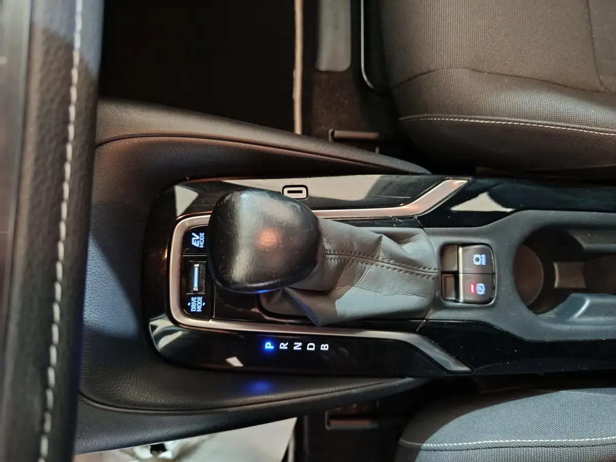 Gros plan sur la console centrale de la Toyota Corolla hybride blanche, montrant le levier de vitesse et les boutons lumineux.