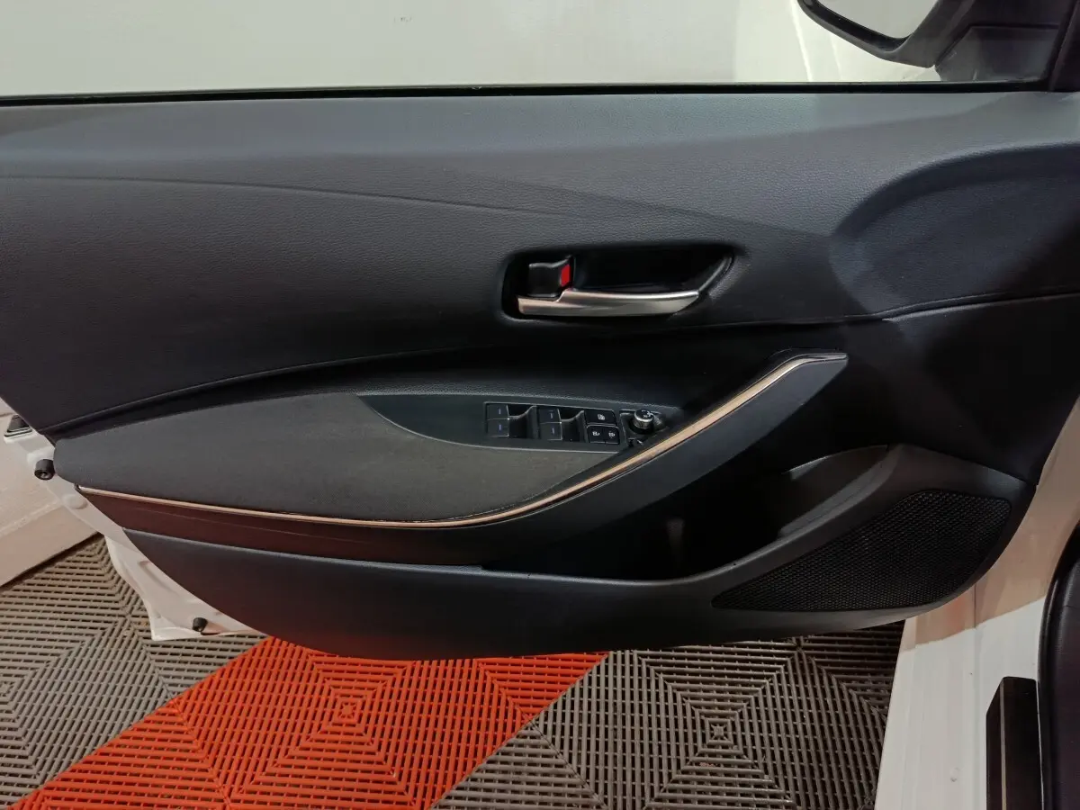 Vue intérieure de la porte avant gauche noire de la Toyota Corolla hybride 2022, avec commandes électriques et poignée chromée.