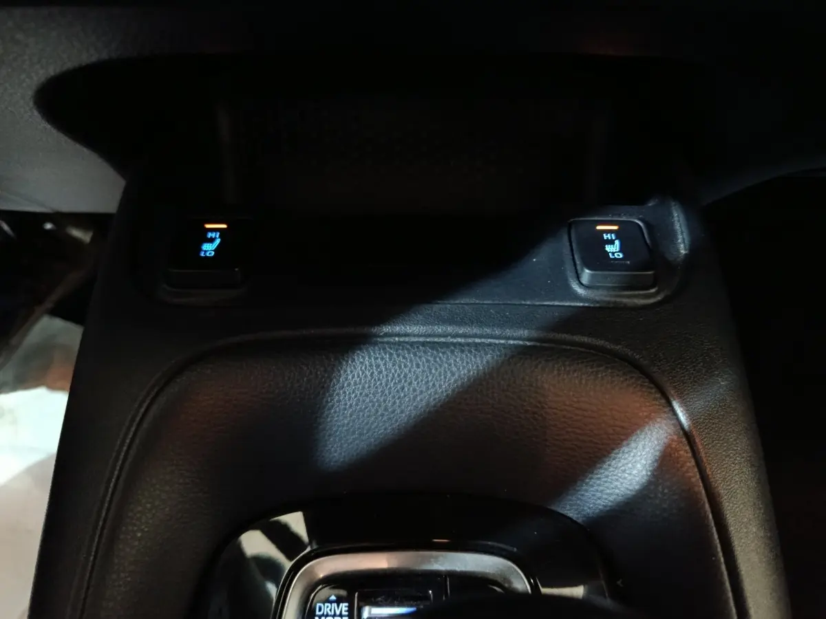 Gros plan sur la console centrale noire avec commandes de sièges chauffants de la Toyota Corolla hybride blanche 2022.