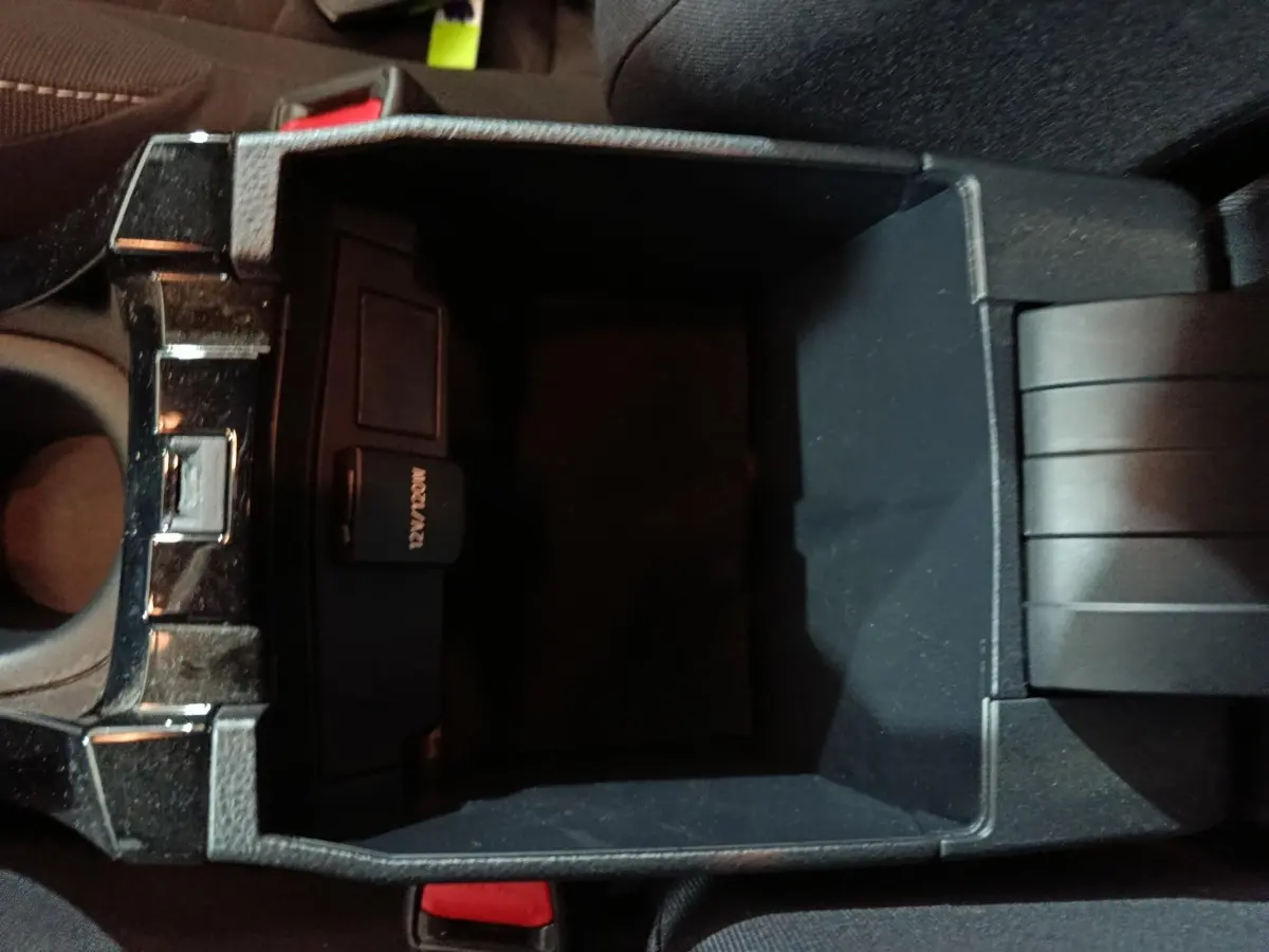 Vue plongeante sur le rangement central noir de la Toyota Corolla hybride 2022, avec prise 12V visible à l'intérieur.