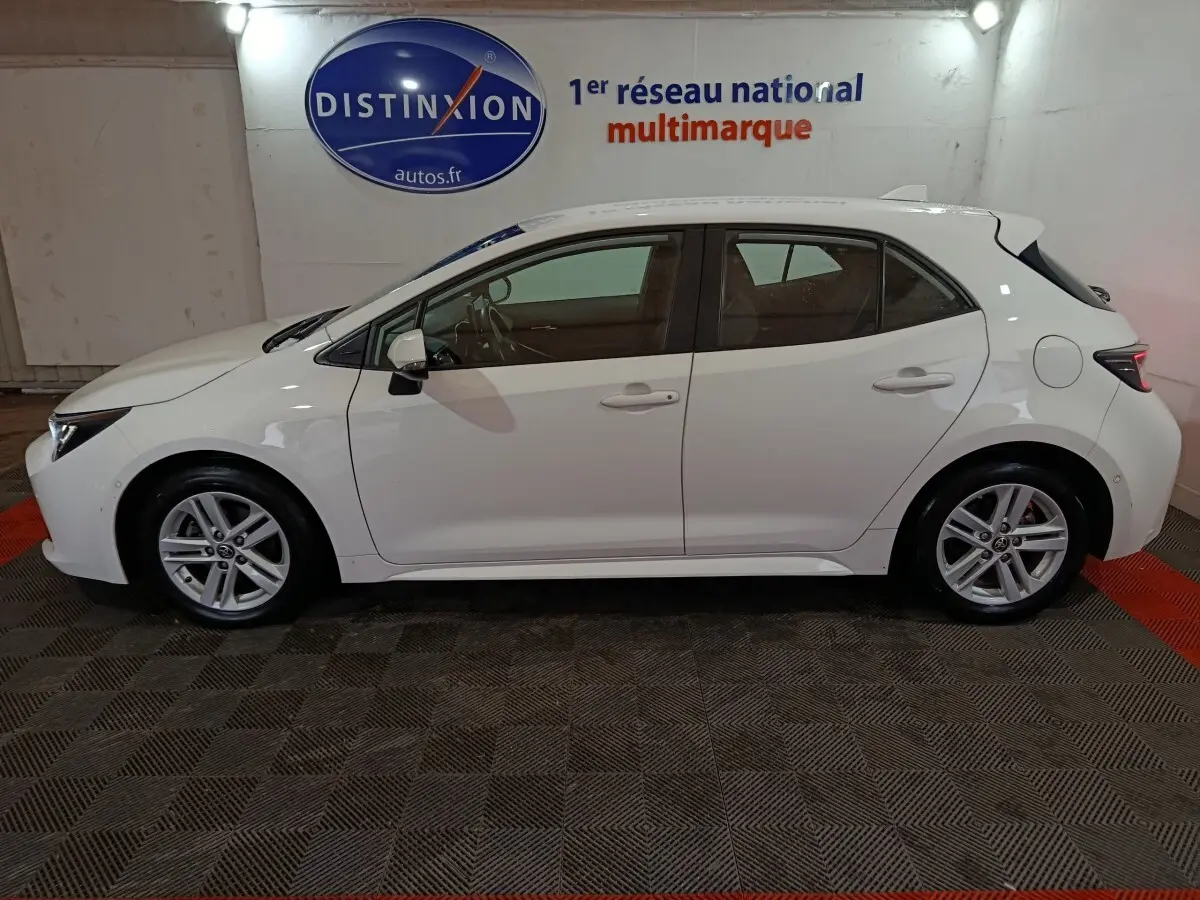 Vue de profil côté gauche d'une Toyota Corolla hybride blanche 2022, avec jantes alliage et rétroviseurs électriques.