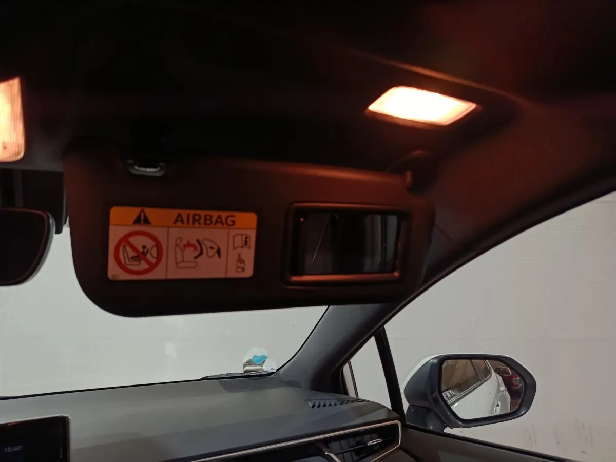 Vue intérieure côté conducteur de la Toyota Corolla hybride blanche, avec pare-soleil et rétroviseur extérieur visibles.