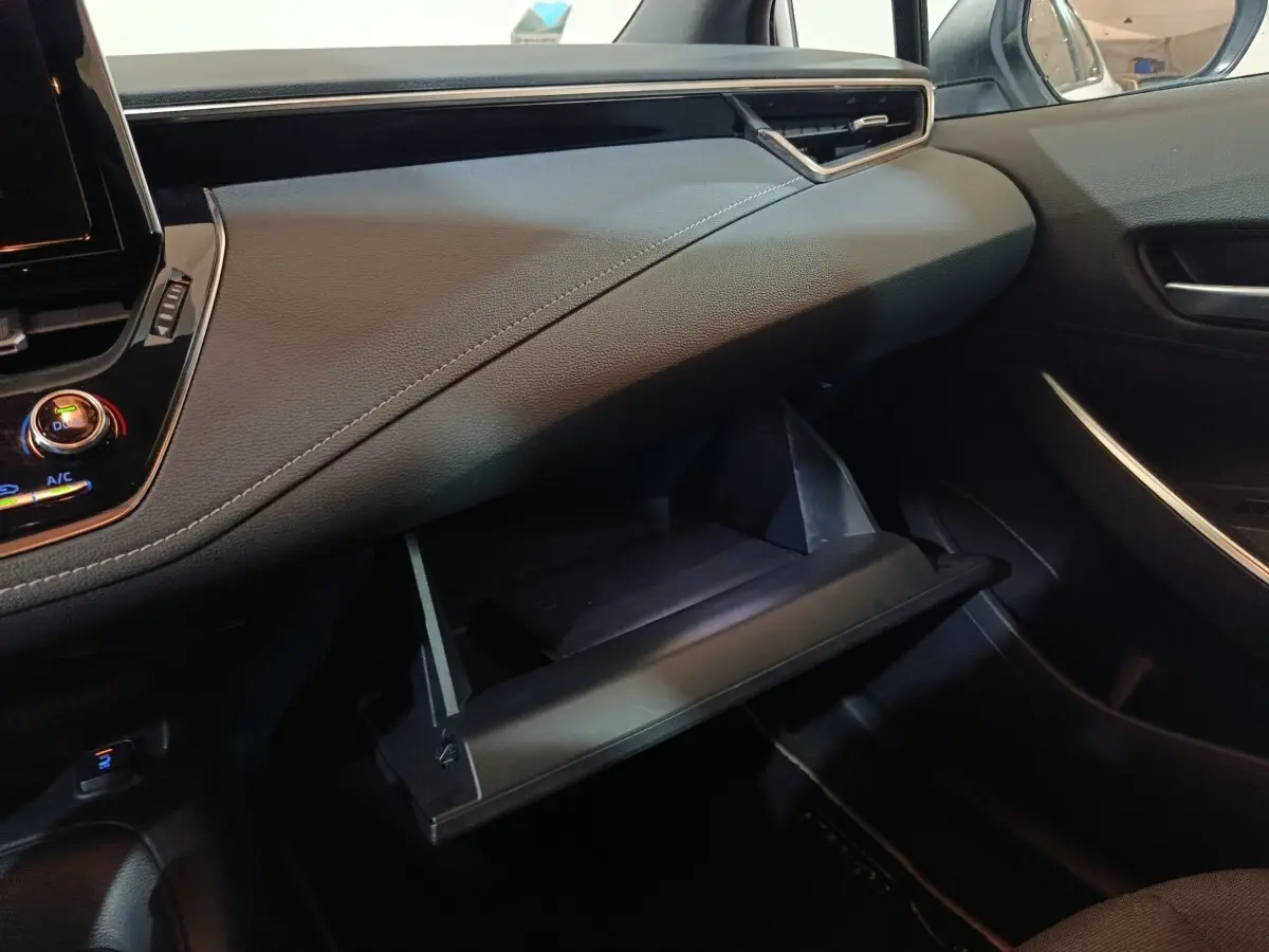 Intérieur de la Toyota Corolla Hybride 2022, vue côté passager sur la boîte à gants ouverte et tableau de bord noir.
