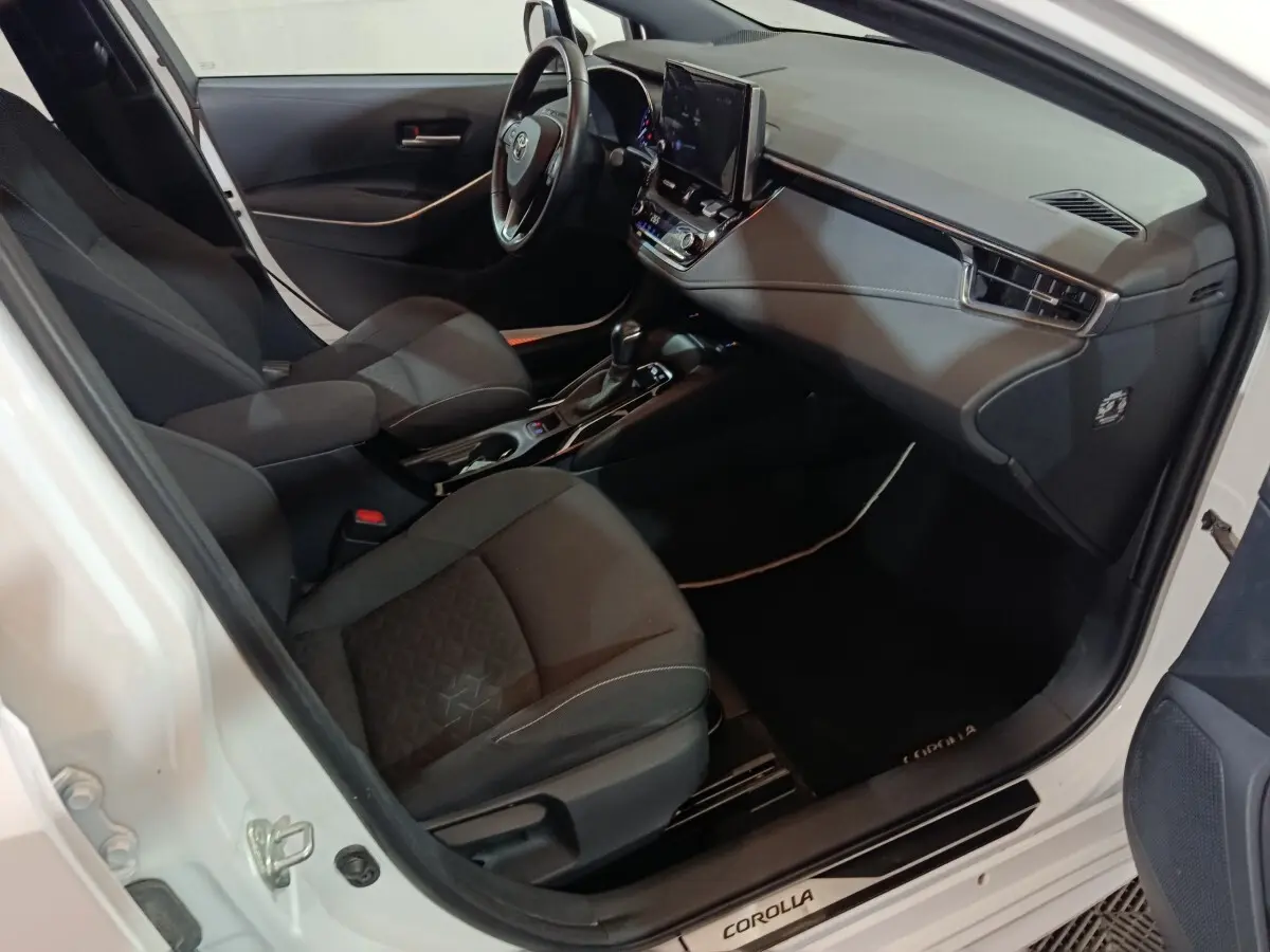 Vue intérieure côté conducteur de la Toyota Corolla hybride blanche 2022, avec tableau de bord moderne et sièges noirs.