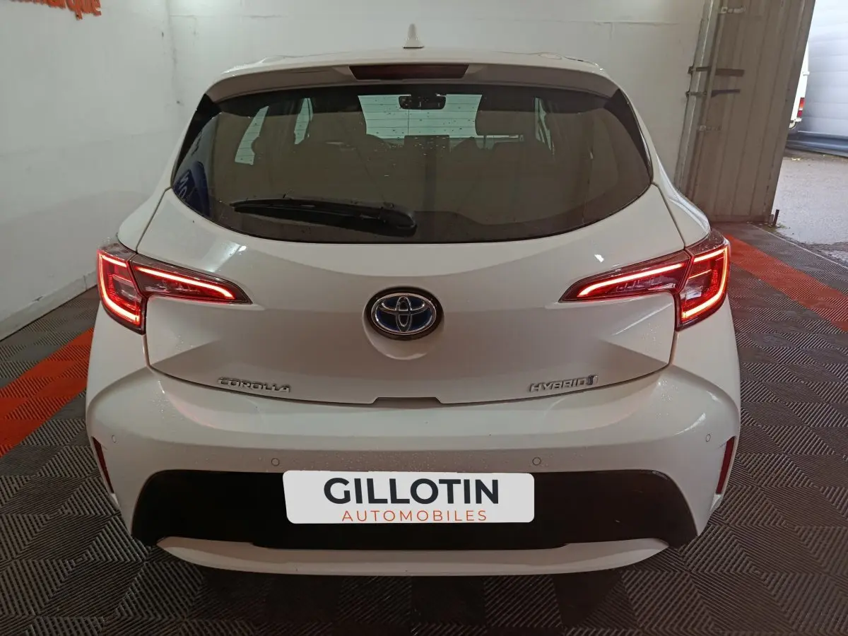 Vue arrière d'une Toyota Corolla hybride blanche avec feux arrière LED allumés dans un garage.