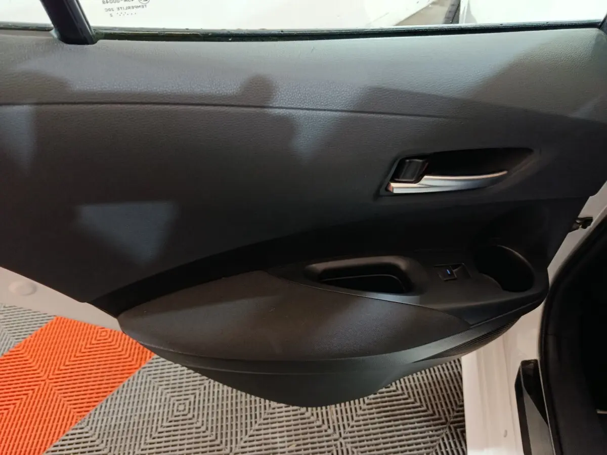 Vue intérieure côté gauche de la porte avant noire d'une Toyota Corolla hybride blanche, avec poignée et commande fenêtre.