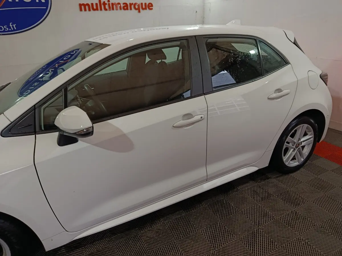 Toyota Corolla hybride blanche vue de profil côté gauche, avec rétroviseur rabattable électriquement visible.