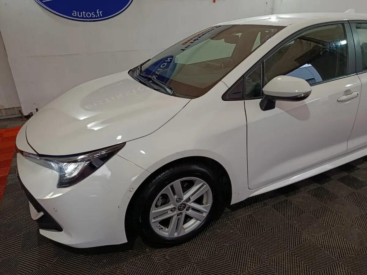 Vue 3/4 avant droit d'une Toyota Corolla hybride blanche avec phares LED et rétroviseurs électriques rabattables.