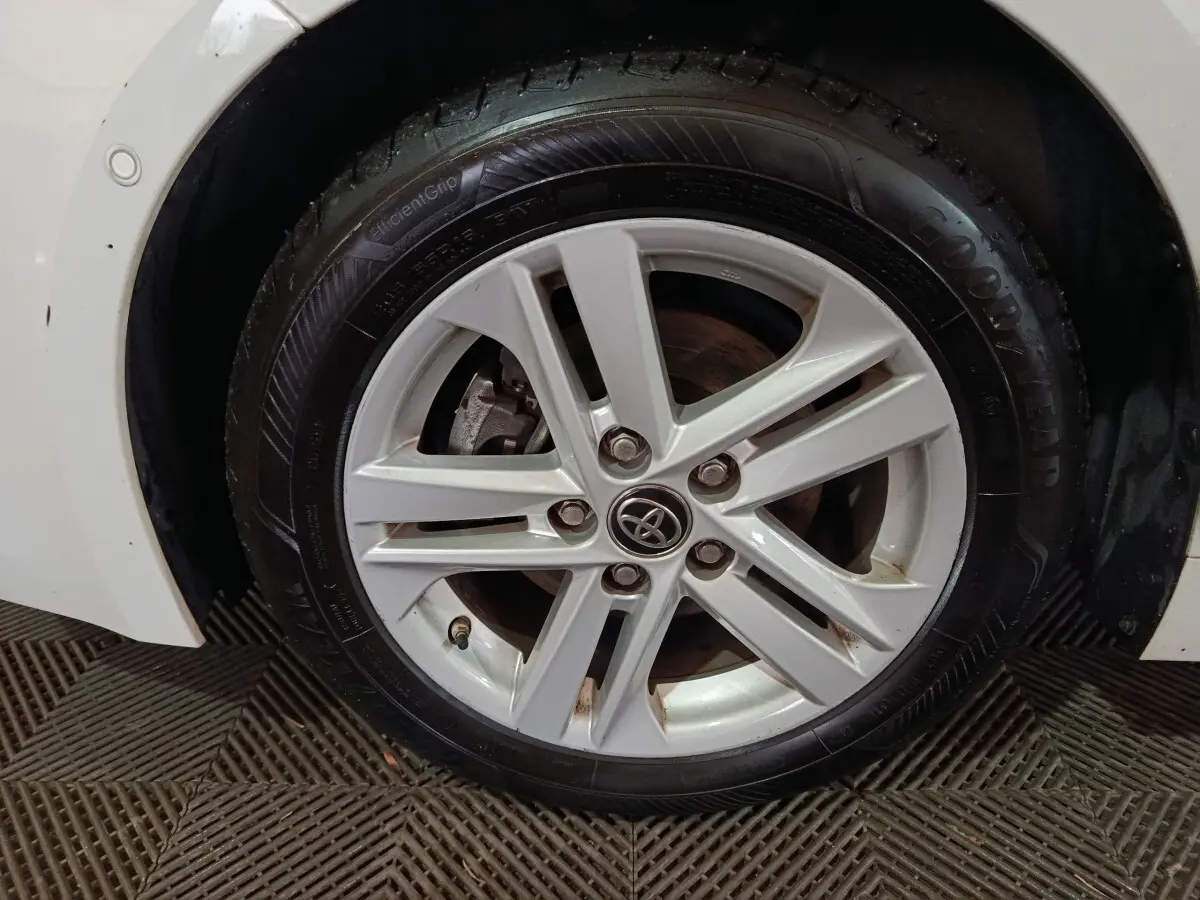 Gros plan sur la roue avant gauche blanche d'une Toyota Corolla hybride avec jante alliage et logo Toyota central.