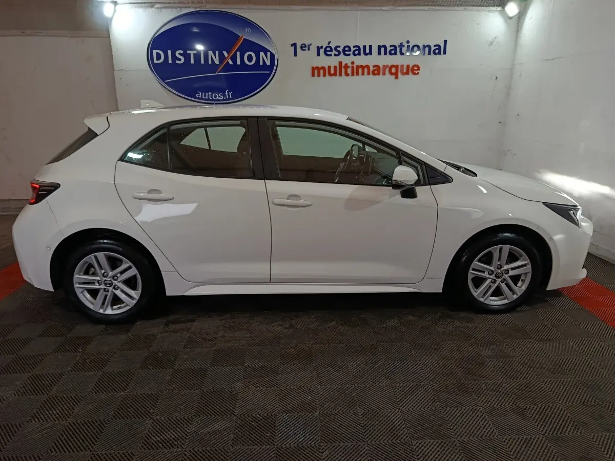 Profil latéral droit d'une Toyota Corolla hybride blanche 2022, avec jantes alliage et rétroviseurs électriques rabattables.