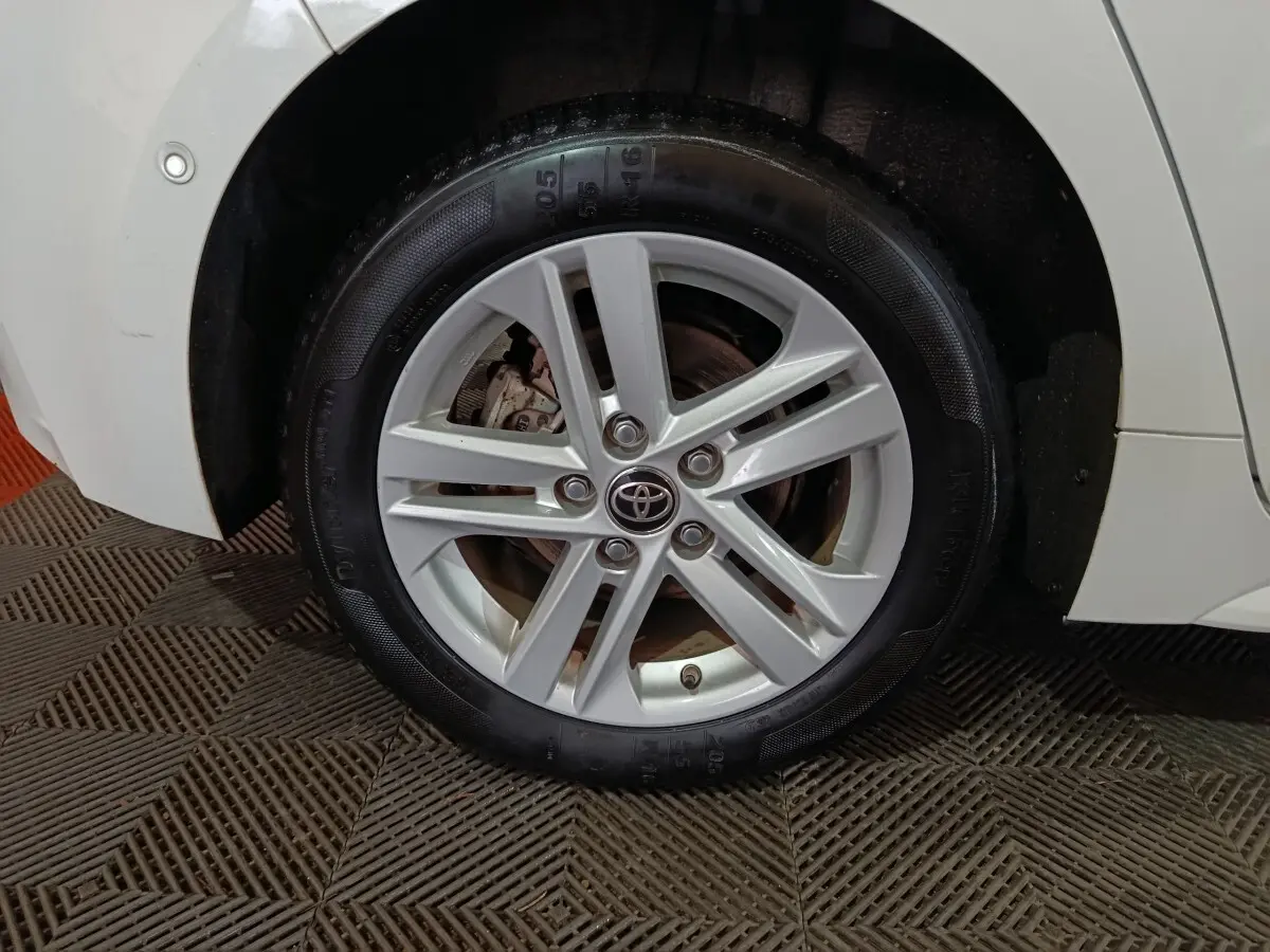 Gros plan sur la roue avant droite blanche de la Toyota Corolla Hybride 2022 avec jante alliage et logo Toyota central.