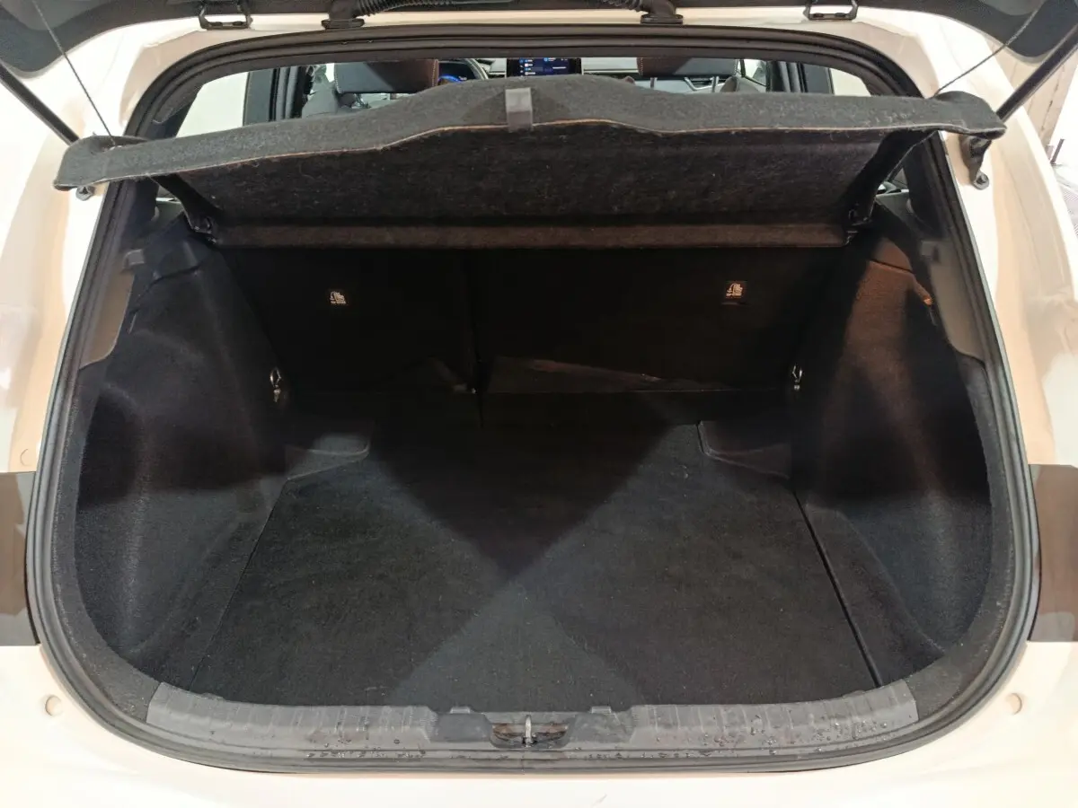 Vue arrière du coffre ouvert d'une Toyota Corolla hybride blanche, montrant l'espace de chargement vide et la tablette cache-bagages.