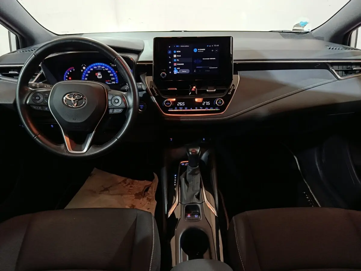 Vue intérieure frontale du tableau de bord et volant cuir noir de la Toyota Corolla Hybride 2022 avec écran tactile central.