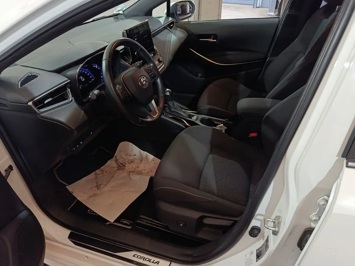 Vue intérieure côté conducteur de la Toyota Corolla hybride blanche 2022, avec tableau de bord et sièges noirs.