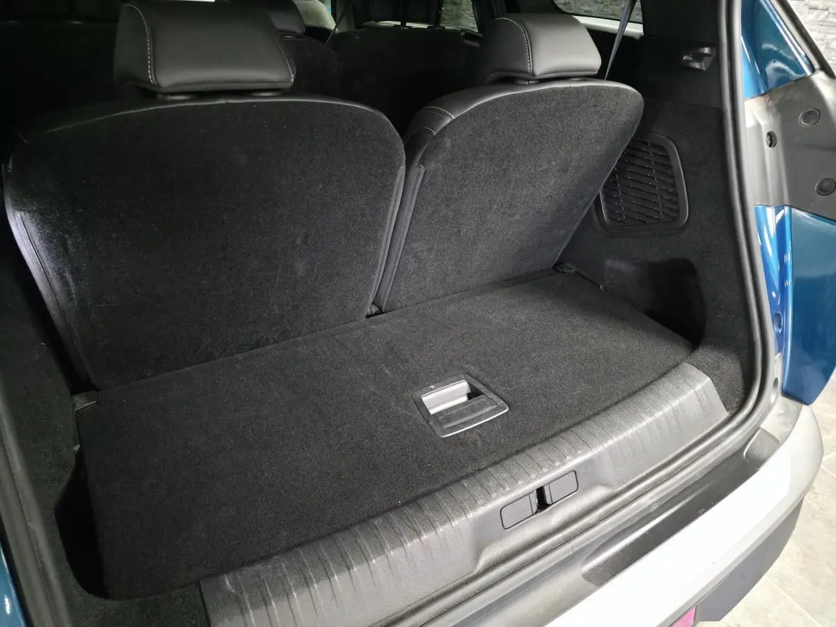 Coffre ouvert vu de l'arrière d'un Peugeot 5008 bleu 2025, banquette arrière partiellement rabattue et intérieur noir.