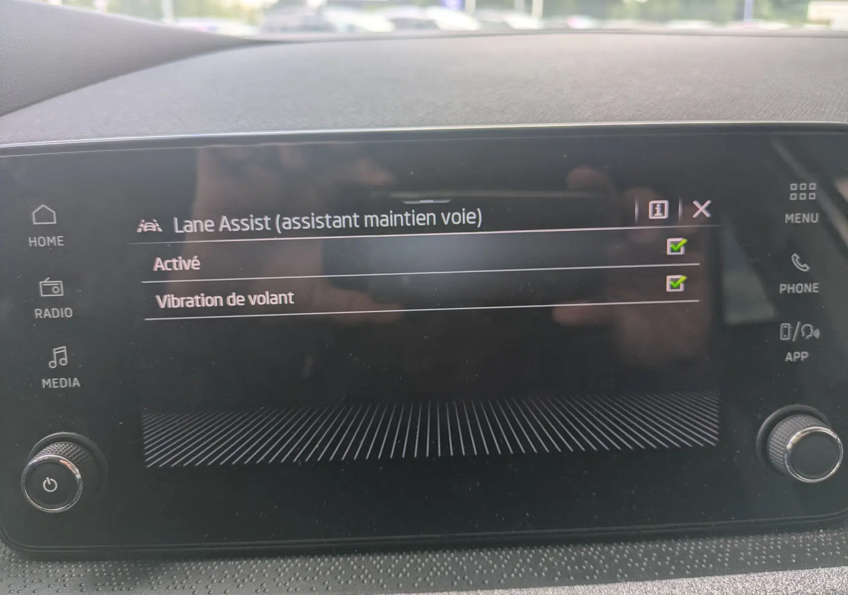 Écran tactile intérieur de la Skoda Scala gris Reflex affichant l'activation de l'assistant maintien de voie avec vibration de volant.