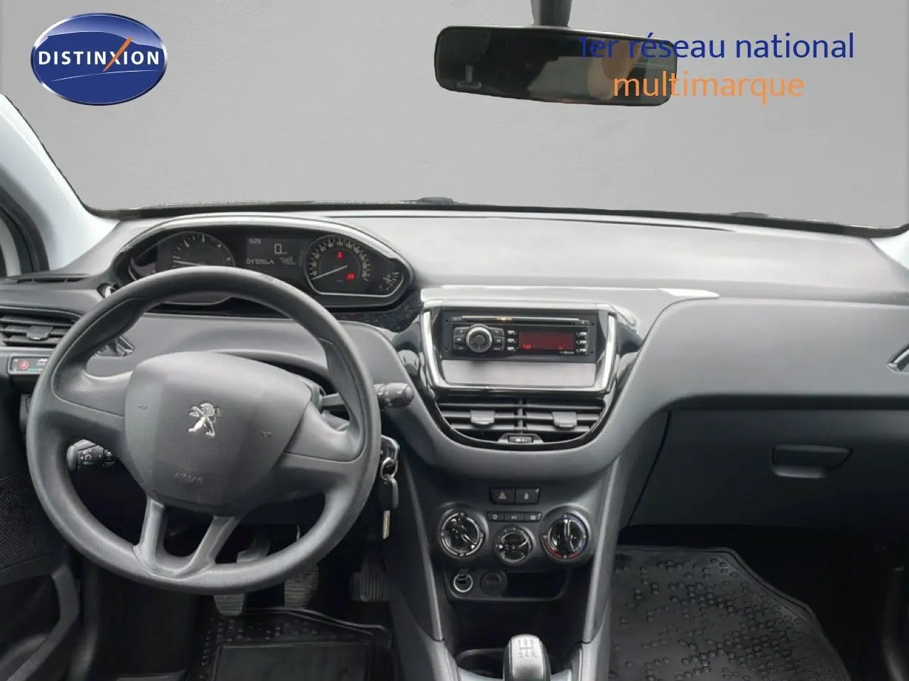 Vue intérieure avant centrée sur le tableau de bord et volant noir d'une Peugeot 208 Société blanc banquise de 2018.