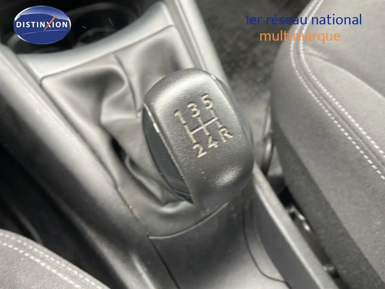 Gros plan sur le levier de vitesses manuel noir de la Peugeot 208 Société blanche, avec coutures visibles sur le siège tissu noir.